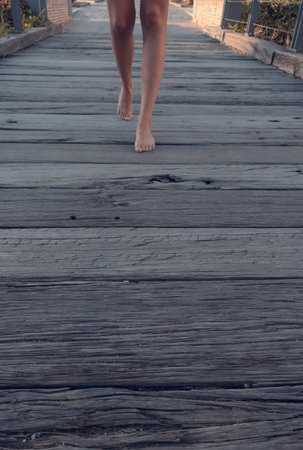 Blonde-haired woman strolling relaxed on wooden bridge de-stressing from city lifeの写真素材