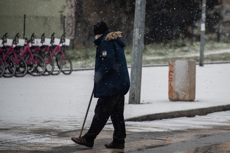 Prague, Czech Republic. 01-12-2021. Old man crossing the avenue on a snowing day with mask during covid-19 from hradcanska tram station at Prague 6のeditorial素材