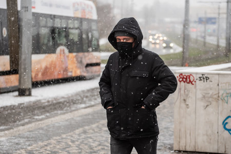 Prague, Czech Republic. 01-12-2021. Man walking to catch the tramway on a snowing day with mask during covid-19 from hradcanska tram station at Prague 6のeditorial素材
