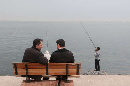 Istanbul, Turkey. 05-23-2018. Two muslim men sitting on a bench talking, where people fish facing the ocean of Istanbul in Turkey.のeditorial素材