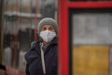 Prague, Czech Republic. 02-08-2021. Old woman with mask and walking stick is looking at the tram schedule in the city center of Prague on a cold winter snowy day.のeditorial素材