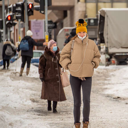 Prague, Czech Republic. 02-08-2021. Young beautiful colorful woman with an old woman behind is walking and talking in the city center of Prague on a cold winter snowy day.のeditorial素材
