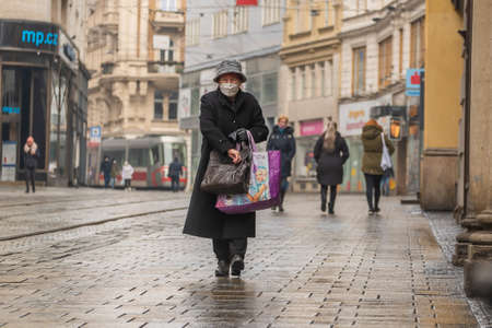 Brno, Czech Republic. 02-17-2021. Old woman with face mask to protect from corona virus walk Masarykova street in the city of Brno on cold winter day.のeditorial素材