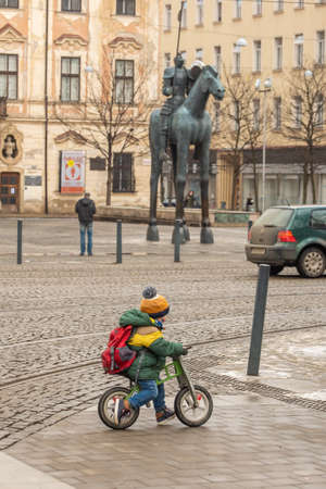 Brno, Czech Republic. 02-17-2021. Child on bike with the horse statue made by Czech artist Jarosla Rona in background close to Church of St. Thomas in city of Brno on winter.のeditorial素材