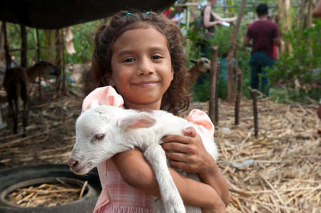 Suchitoto, El Salvador. 06-25-2016. Girl holding a baby goat at the house where they live in the rural area. She helps their parents in the everyday duties.のeditorial素材
