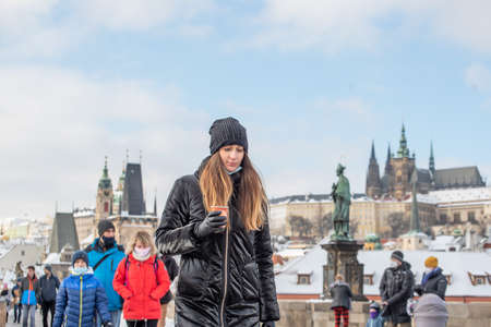 Prague, Czech Republic. 02-23-2021. Young beautiful and trendy tourist woman in the city center of Prague drinking coffee on the Charles Bridge, enjoying a cold day during winterのeditorial素材