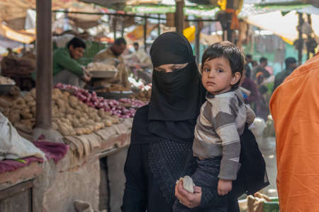 Jaipur, India. 09-05-2018. Muslim woman with wail dress in black carrying her child is walking in the local market in the center of Jaipur.のeditorial素材