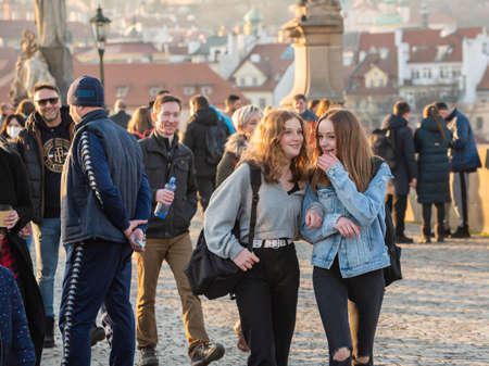 Prague, Czech Republic. 03-02-2021. Two young beautiful women walking, talking and having good fun on the Charles Bridge in the city center of Prague on a beautiful sunset during winter.のeditorial素材