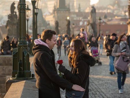 Prague, Czech Republic. 03-02-2021. Romantic couple with flower talking and having good fun on the Charles Bridge in the city center of Prague on a beautiful sunset during winter.のeditorial素材