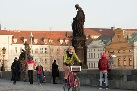 Prague, Czech Republic. 03-02-2021. Old man riding on a bicycle on the Charles Bridge in the city center of Prague during winter with a beautiful sunset.のeditorial素材