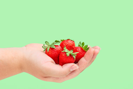beautiful vivrant shot of a girl's hand holding cuite juicy strawberries on a green background,...