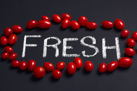 fun shot of the word fresh written with chalk surrounded by healthy fresh vibrant red cherry tomatoes on a blackboard, concept eating fresh healthy locally produced produceの写真素材