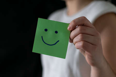 Hand holding green paper cut happy smile face on black background , positive thinking, mental health assessment , world mental health day conceptの写真素材