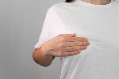 Woman in white t-shirt suffering from back pain on gray backgroundの写真素材