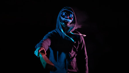 Young man in hoodie and mask with glowing skull on black backgroundの写真素材