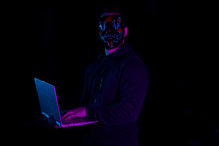 Portrait of a man in a mask with a laptop on a dark backgroundの写真素材