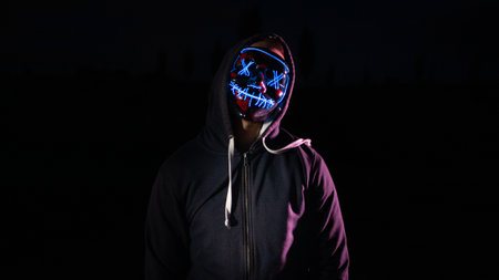 Hooded man in a black hoodie with a neon skull on his face