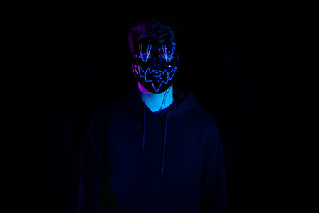 Man in hoodie with neon mask on black background. halloween conceptの写真素材