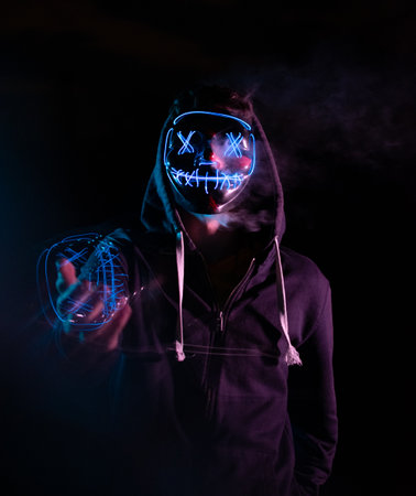 Man in dark hoodie with glowing skull and bones on dark background