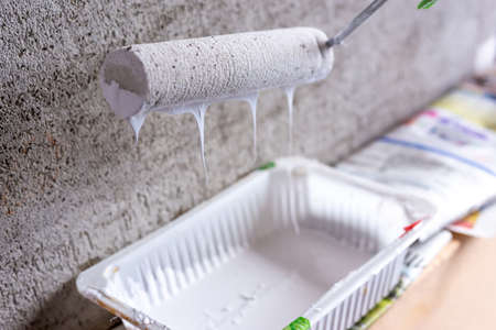 Cement wall painting with white paint and roller. Yellow gloves.の写真素材