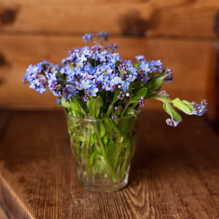 Blue wildflowers in a glass cup on a wooden background. Forget me nots.の写真素材