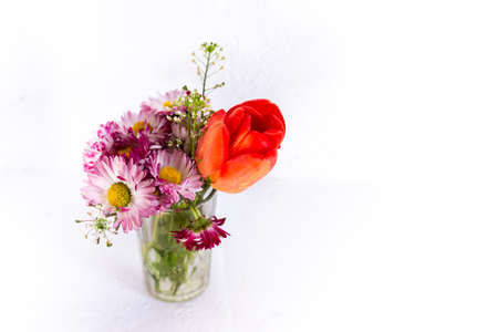 Tulip and pink flowers in a glass cup on a white background.の写真素材