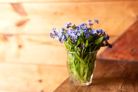 Blue wildflowers in a glass cup on a wooden background. Forget me nots.の写真素材