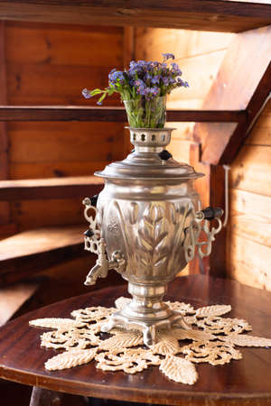 Old metal samovar and a bouquet of blue flowers on a wooden backgroundの写真素材