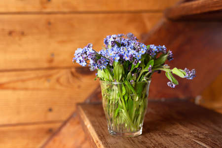 Blue wildflowers in a glass cup on a wooden background. Forget me nots. High quality photoの写真素材