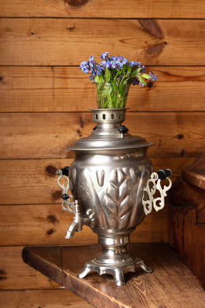 Old metal samovar and a bouquet of blue flowers on a wooden backgroundの写真素材