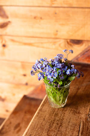 Blue wildflowers in a glass cup on a wooden background. Forget me nots.の写真素材