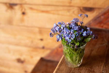 Blue wildflowers in a glass cup on a wooden background. Forget me nots.の写真素材