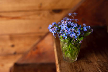Blue wildflowers in a glass cup on a wooden background. Forget me nots.の写真素材