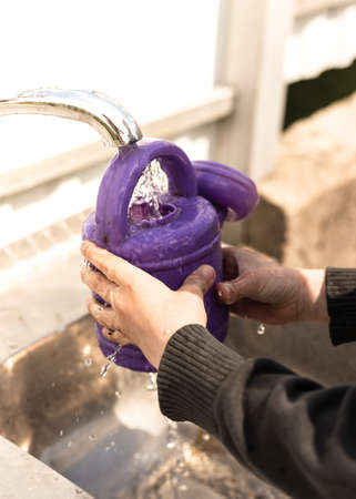 The boy pours water from a tap into a purple watering can. High quality photoの写真素材