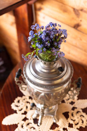 Old metal samovar and a bouquet of blue flowers on a wooden backgroundの写真素材