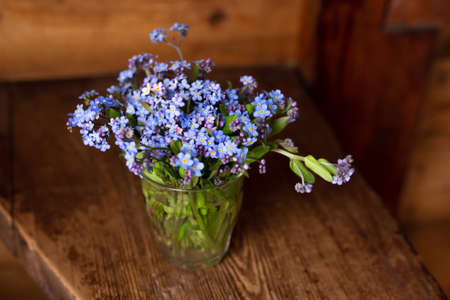 Blue wildflowers in a glass cup on a wooden background. Forget me nots.の写真素材