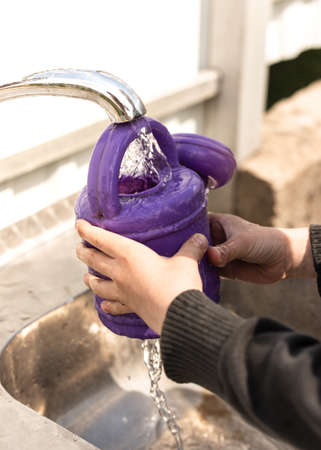 The boy pours water from a tap into a purple watering canの写真素材