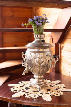 Old metal samovar and a bouquet of blue flowers on a wooden backgroundの写真素材
