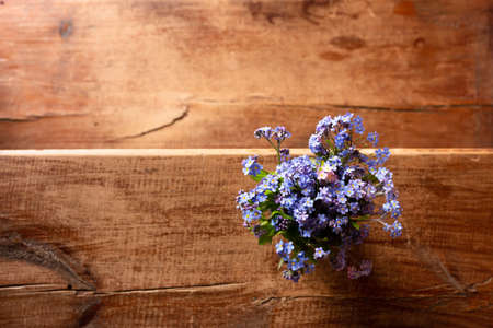 Blue wildflowers in a glass cup on a wooden background. Forget me nots.の写真素材