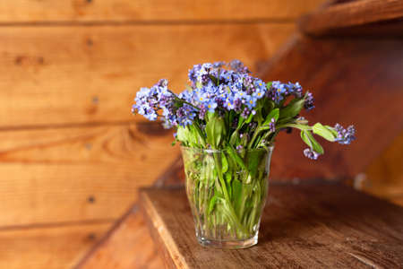 Blue wildflowers in a glass cup on a wooden background. Forget me nots.の写真素材