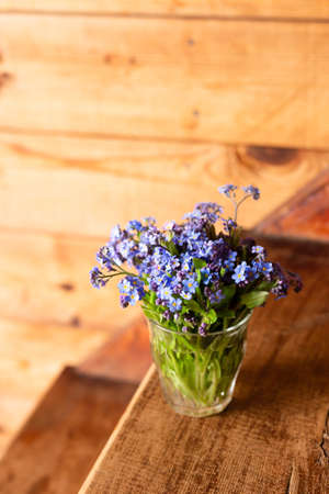 Blue wildflowers in a glass cup on a wooden background. Forget me nots.の写真素材