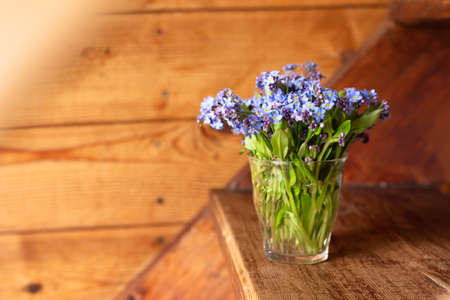 Blue wildflowers in a glass cup on a wooden background. Forget me nots.の写真素材