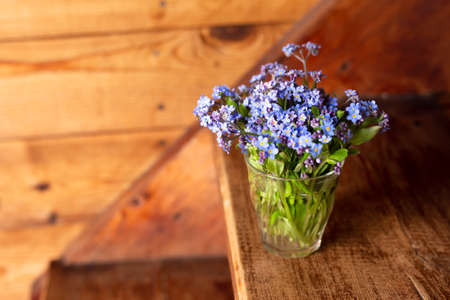 Blue wildflowers in a glass cup on a wooden background. Forget me nots.の写真素材