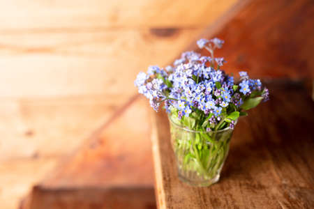 Blue wildflowers in a glass cup on a wooden background. Forget me nots.の写真素材