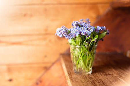 Blue wildflowers in a glass cup on a wooden background. Forget me nots.の写真素材