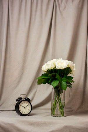 Bouquet of white roses in a vase and a clock on a gray background