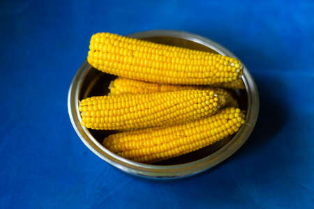 Boiled corn in an iron bowl on a blue background