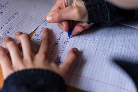 The boy writes in a notebook. The child is doing homework. Pen and notebook.