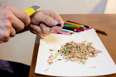 A man sharpens a pencil with a stationery knife