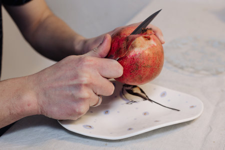 Man peels a pomegranate fruit with a knife on a plateの写真素材